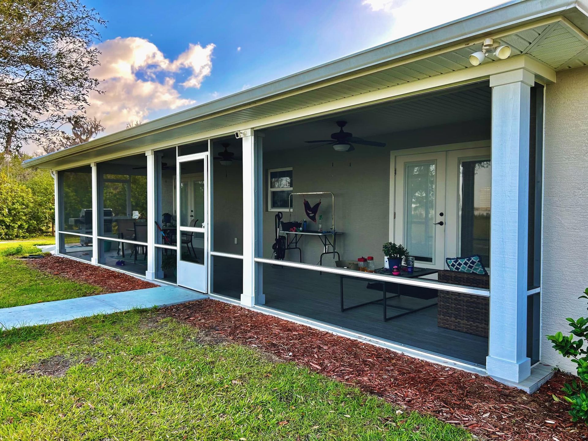 Screened-in porch attached to a house; white frame, gray walls, blue accents, outdoor furniture visible.