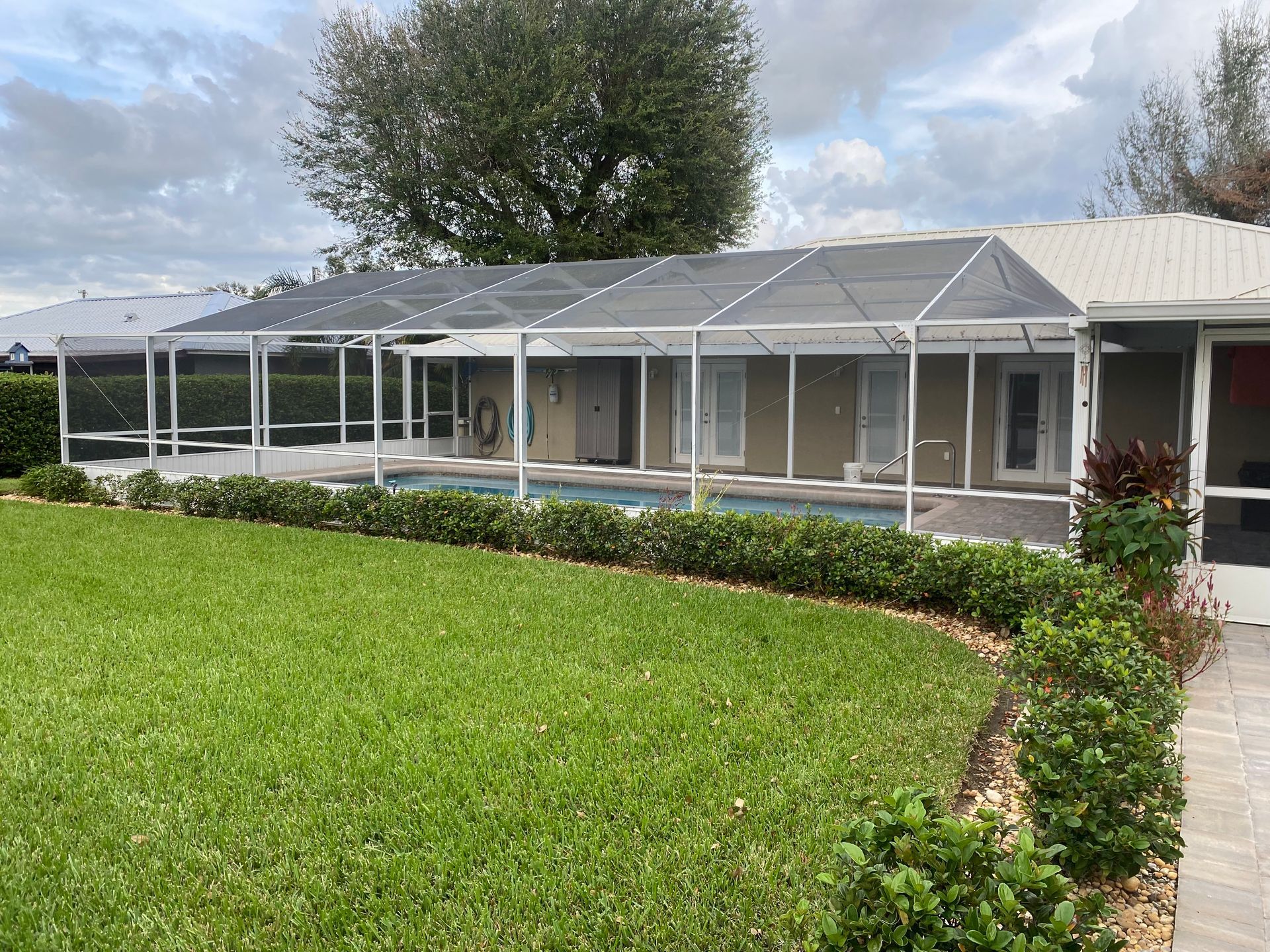 A screened-in pool enclosure with a pool, lawn, and house under a cloudy sky.