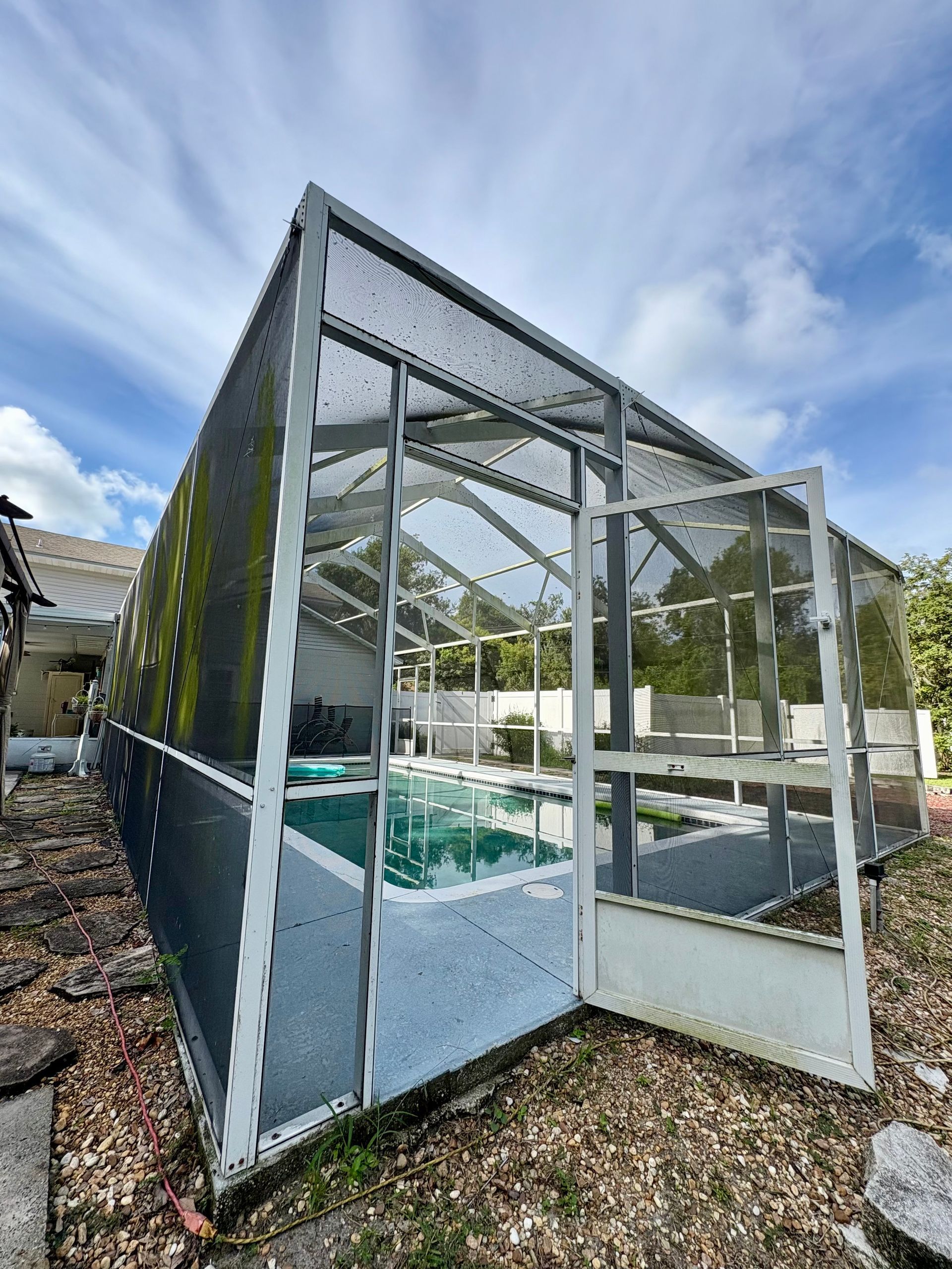 Pool enclosure with open door; screen walls and roof, green pool inside.