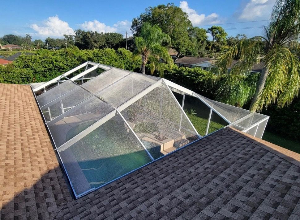Pool enclosure with roof, screened sides, brown roof shingles, and green surrounding foliage.