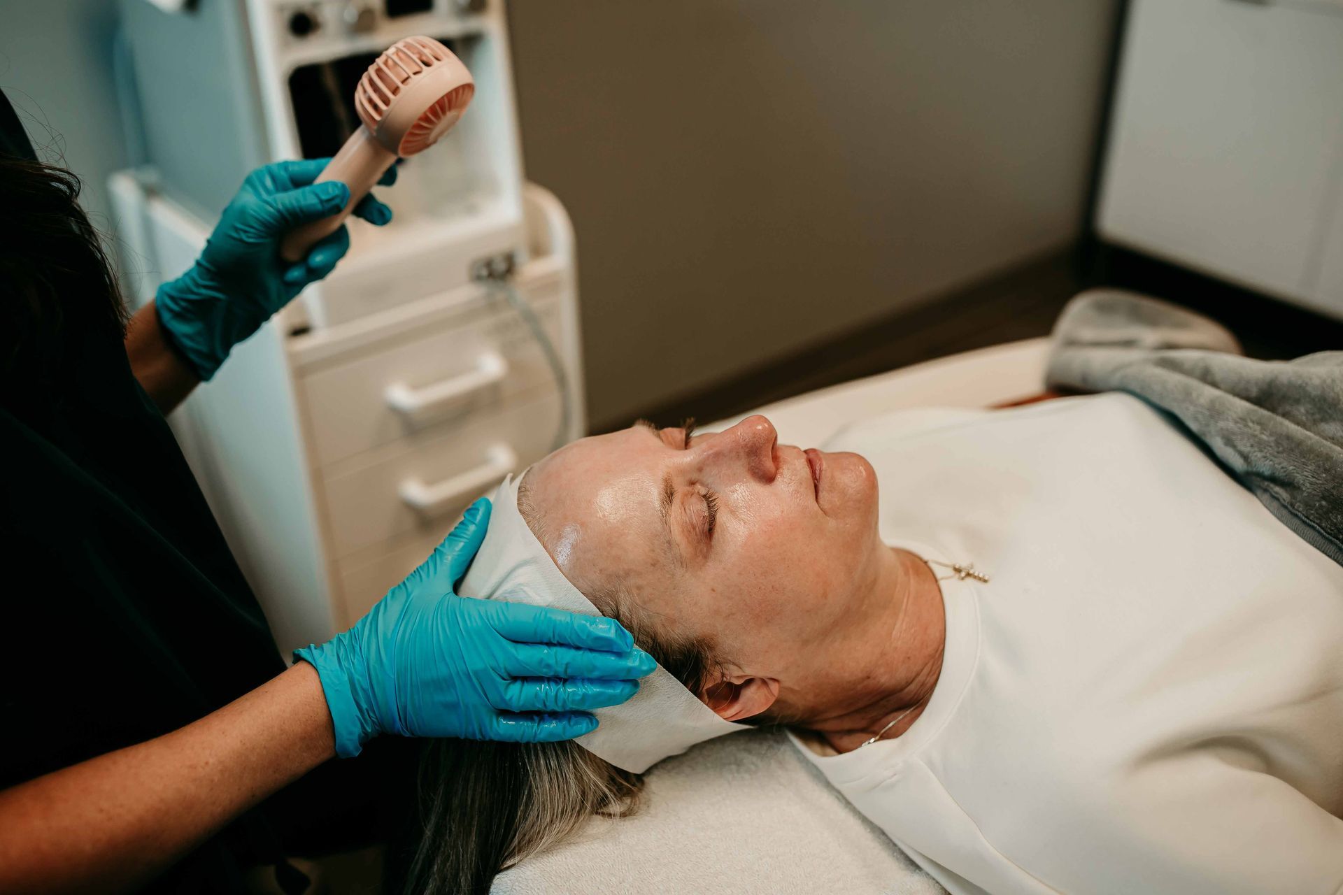Person receiving a facial treatment in a spa, with a technician holding a small fan.