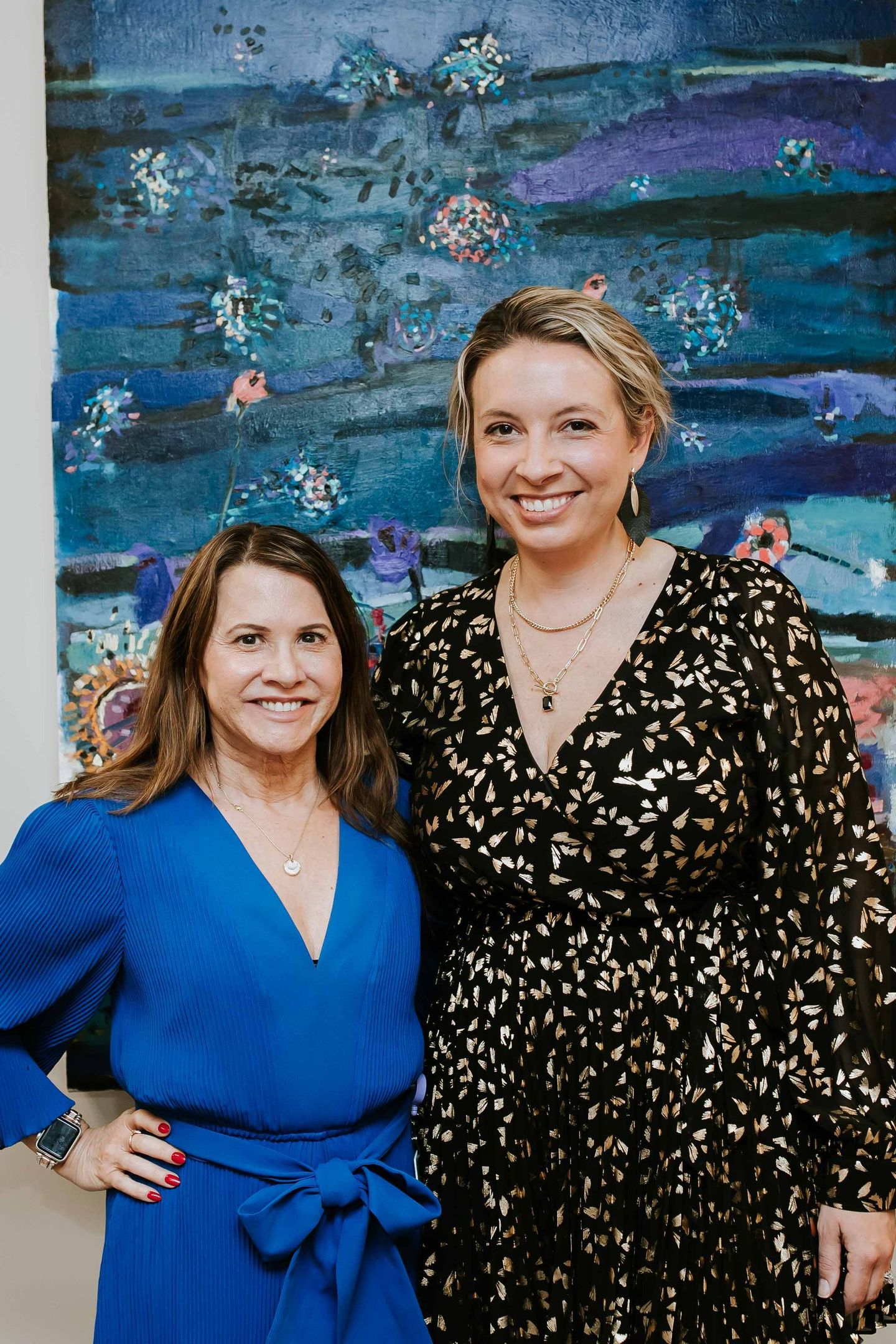 Two women are posing for a picture in front of a painting.