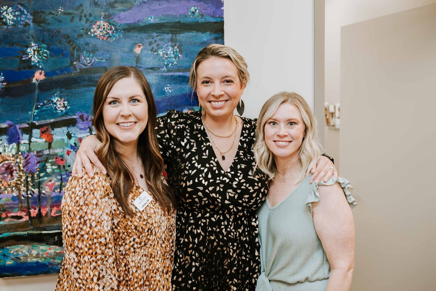 Three women are posing for a picture in front of a painting.