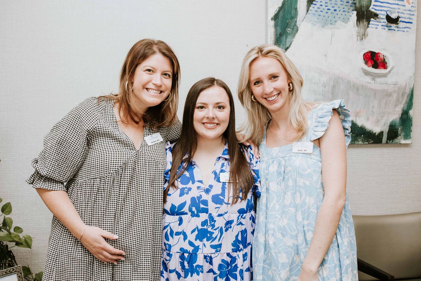 Three women are posing for a picture together in front of a painting.