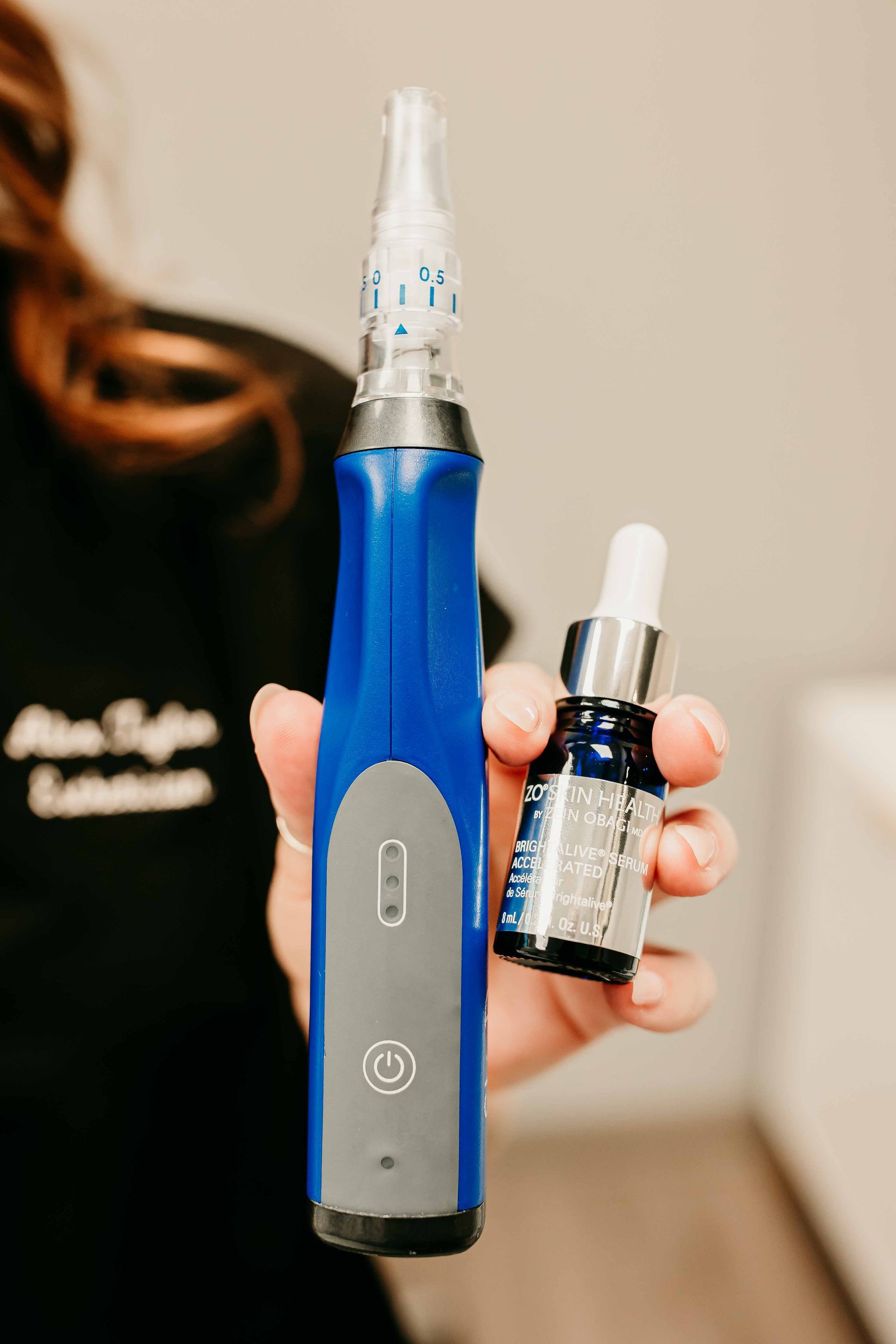 A person holding a blue microneedling device and a small dropper bottle in a professional skincare setting.