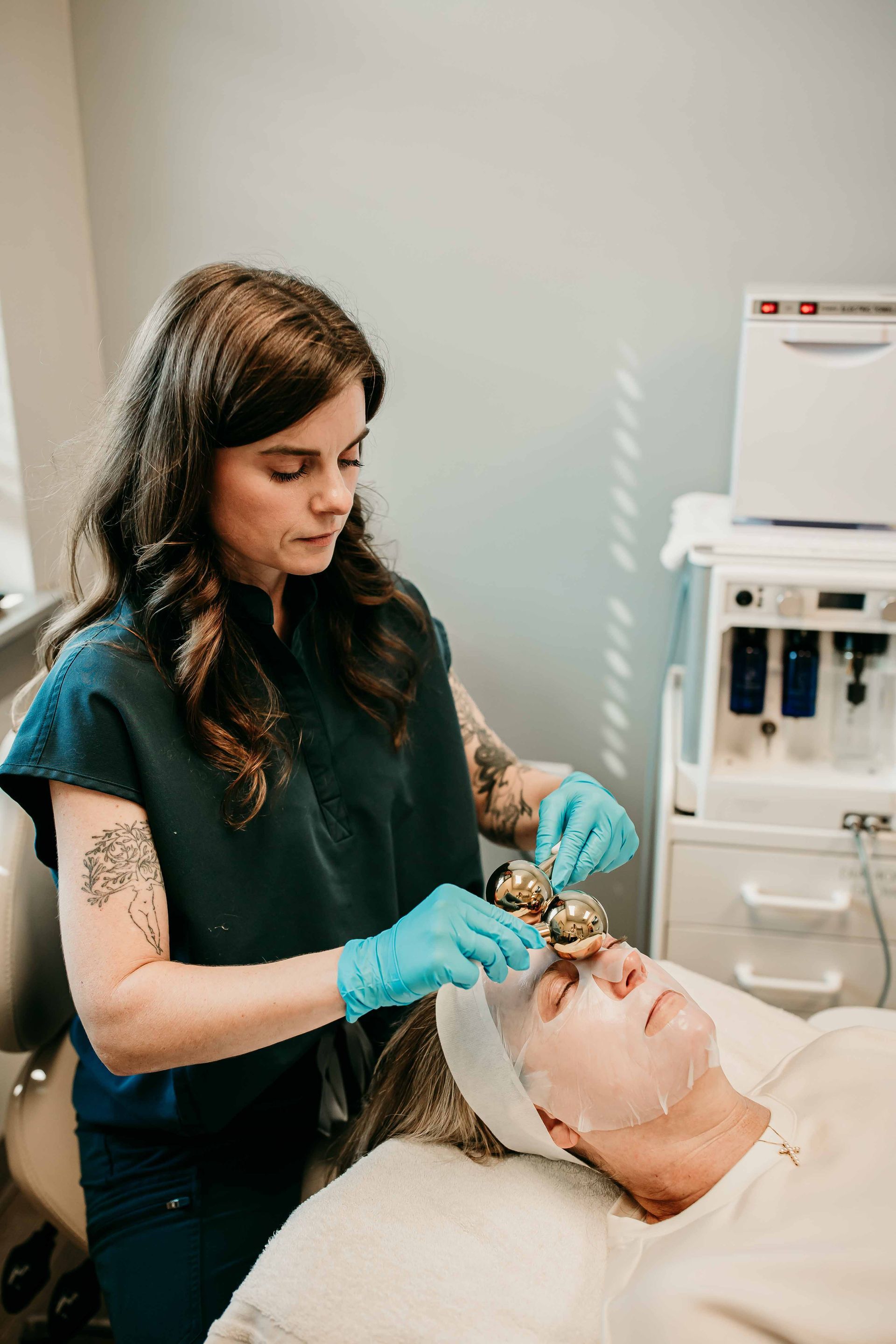 Esthetician performing facial treatment with massage tools. Clinic setting.