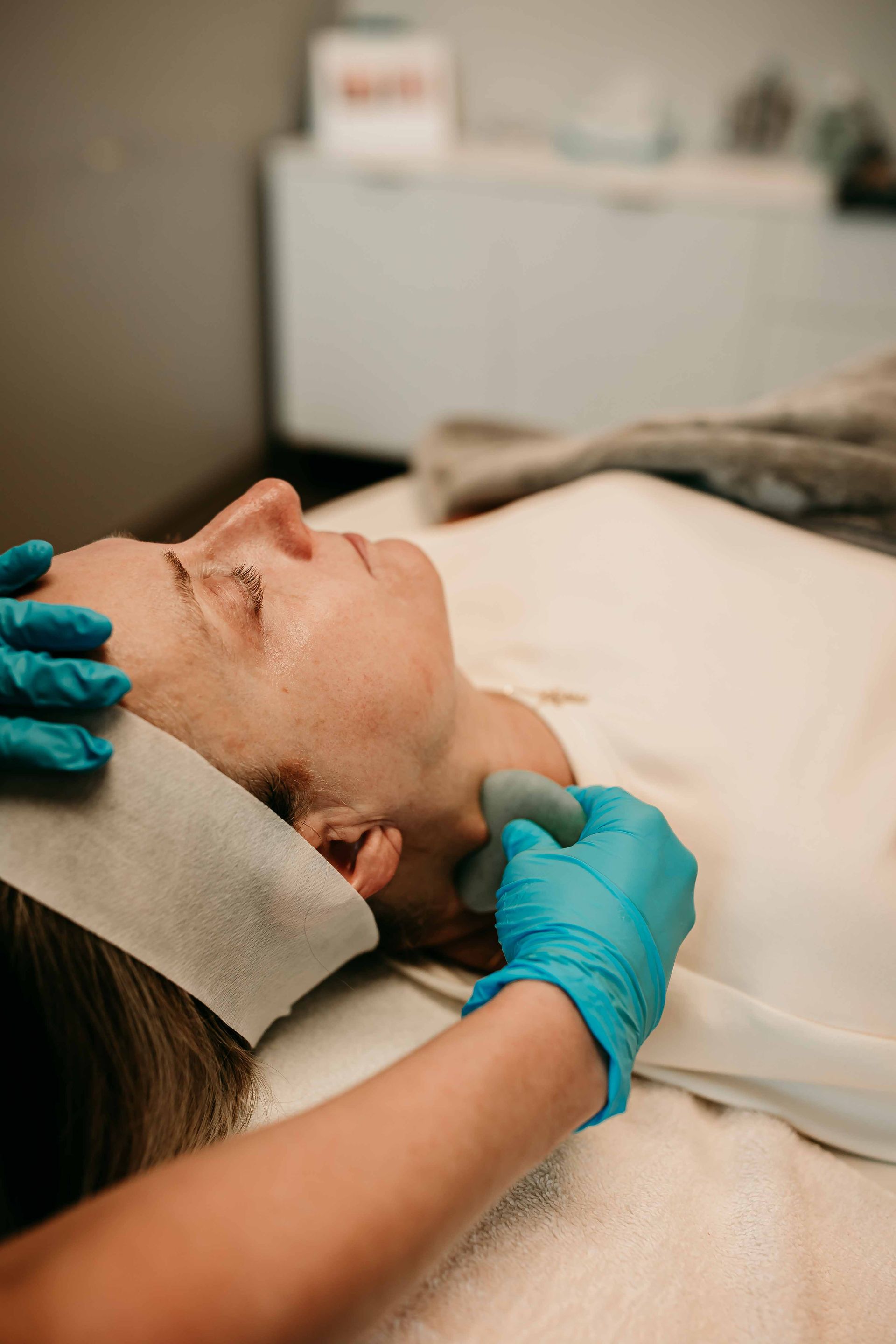 Person receiving facial treatment with a scraping tool. Hands in blue gloves.