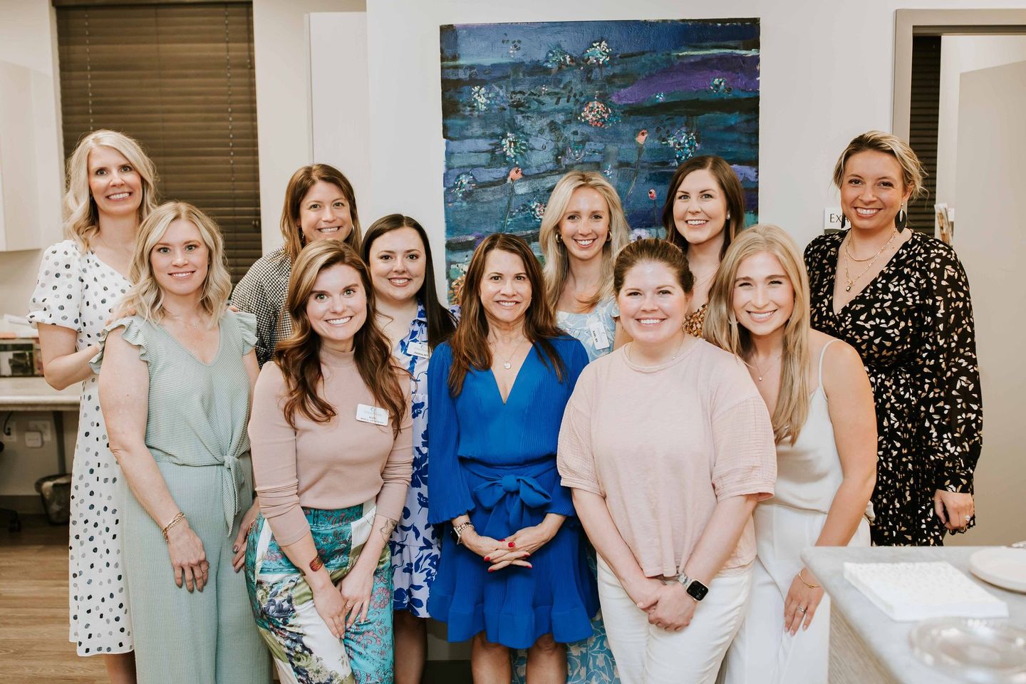 A group of women are posing for a picture in front of a painting.