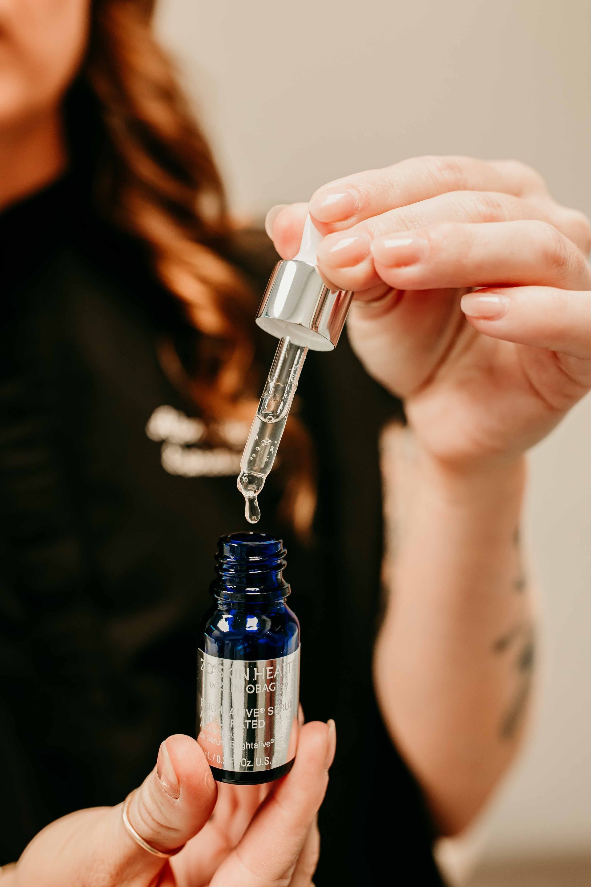 A person holds a small blue glass dropper bottle, dispensing a liquid into the open container.