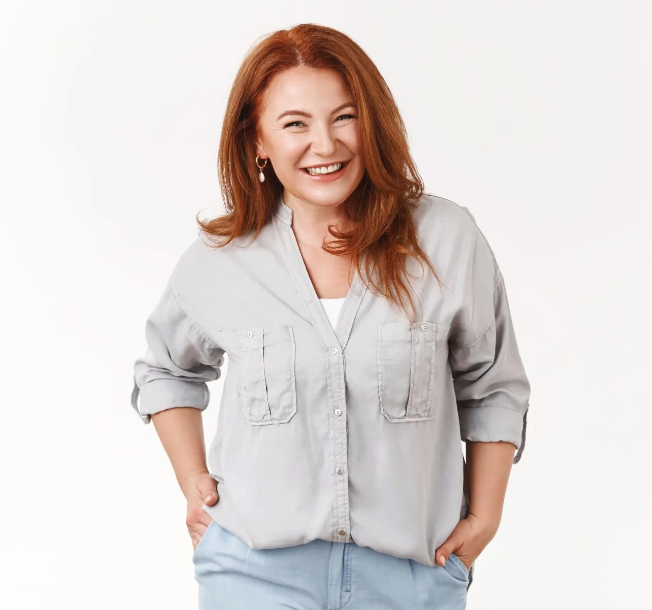 A woman with red hair is wearing a grey shirt and blue shorts and smiling.