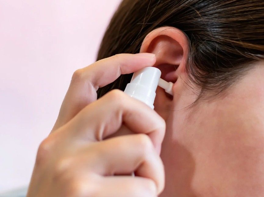 woman showing how to spray olive oil into an ear before an ear wax removal appointment