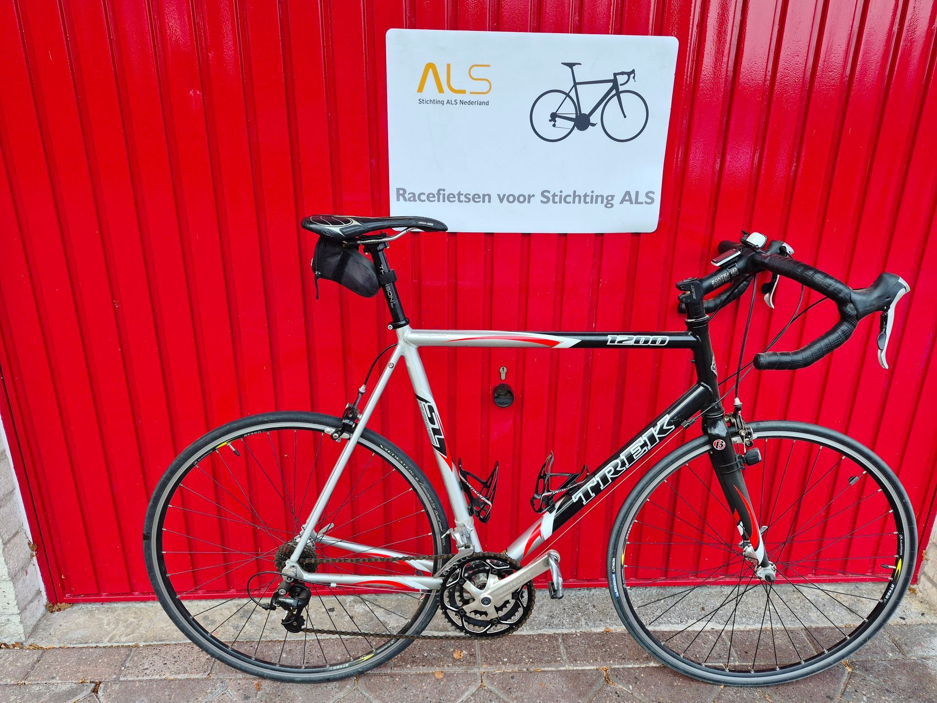Racefiets voor een rode muur met bord.