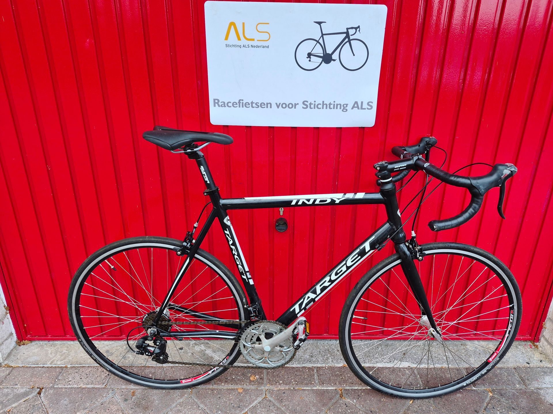 Black road bike in front of a red door, with a sign reading