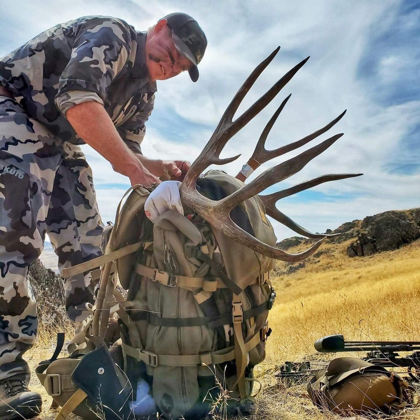 A man in a camo uniform is putting antlers in a backpack