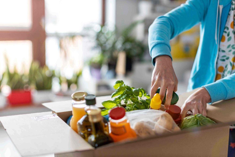 A Woman is Opening a Cardboard Box Filled With Groceries — Howard Springs Supermarket In Howard Springs, NT