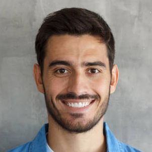 Smiling man with dark hair and beard against a gray background, wearing a blue shirt