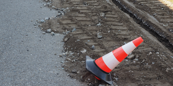 An orange and white traffic cone is sitting on the side of a road.