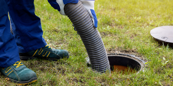 A man is pumping a hose into a septic tank.