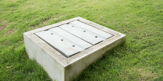 A concrete manhole cover is sitting in the middle of a lush green field.
