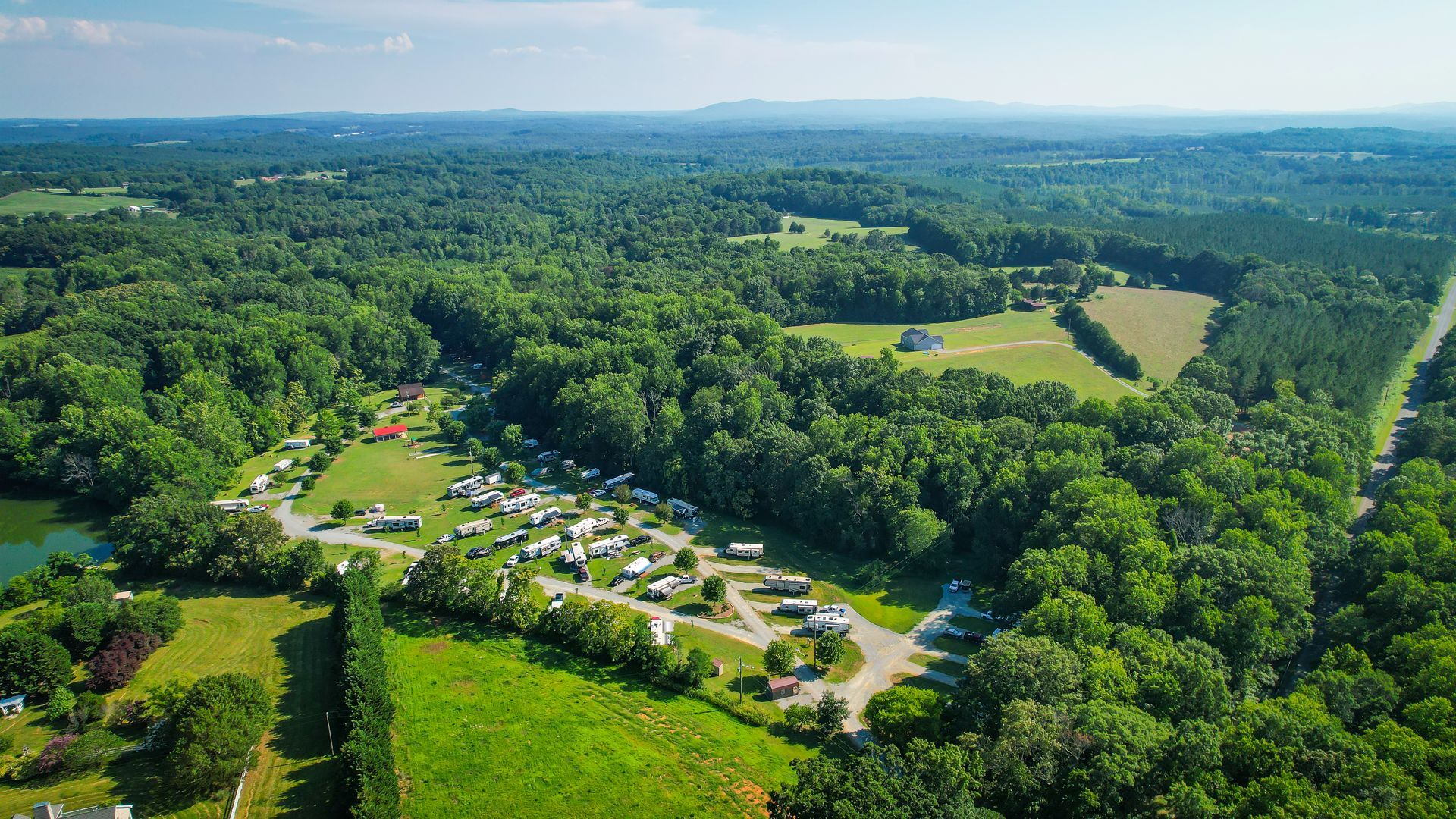 Aerial view of a campsite surrounded by green trees, with trailers, and a road.