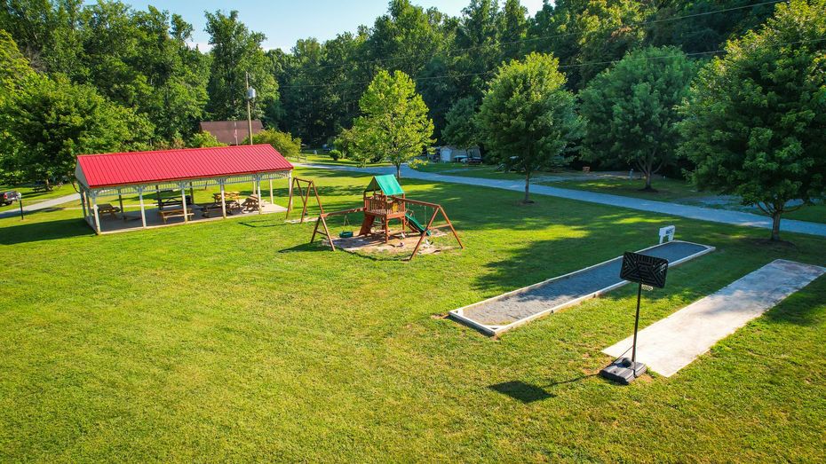 Park with playground, picnic shelter, horseshoe pits, and trees under a sunny sky.