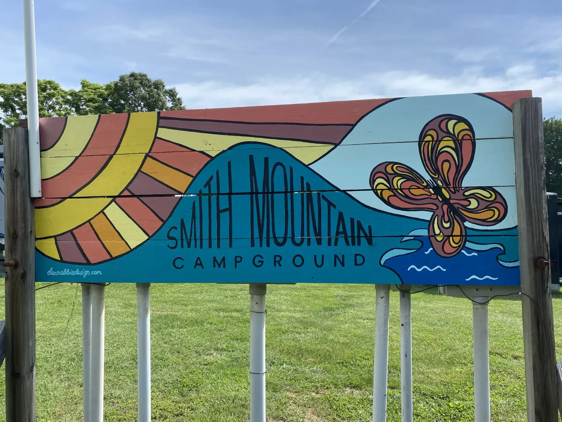 Sign for Smith Mountain Campground; colorful painted sun, mountains, water, and an abstract flower.