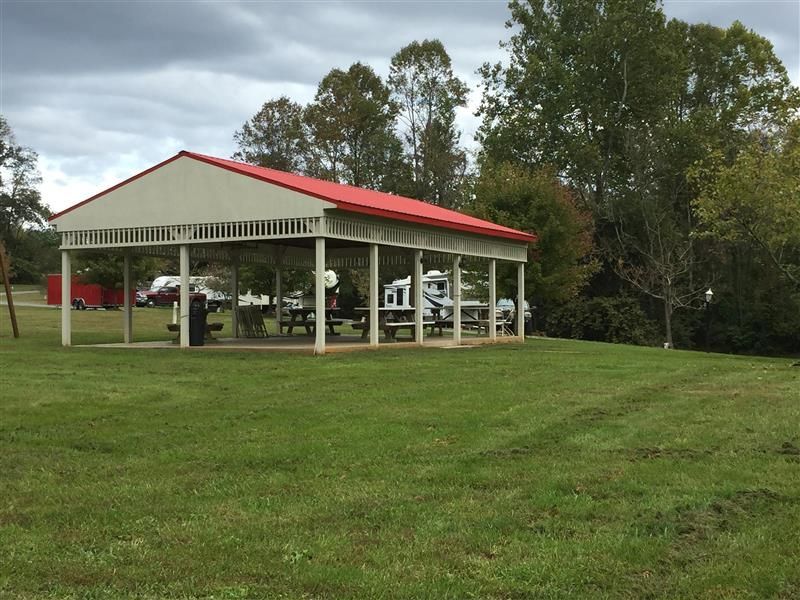 Picnic shelter with red roof in a grassy park; RVs and picnic tables are visible inside.