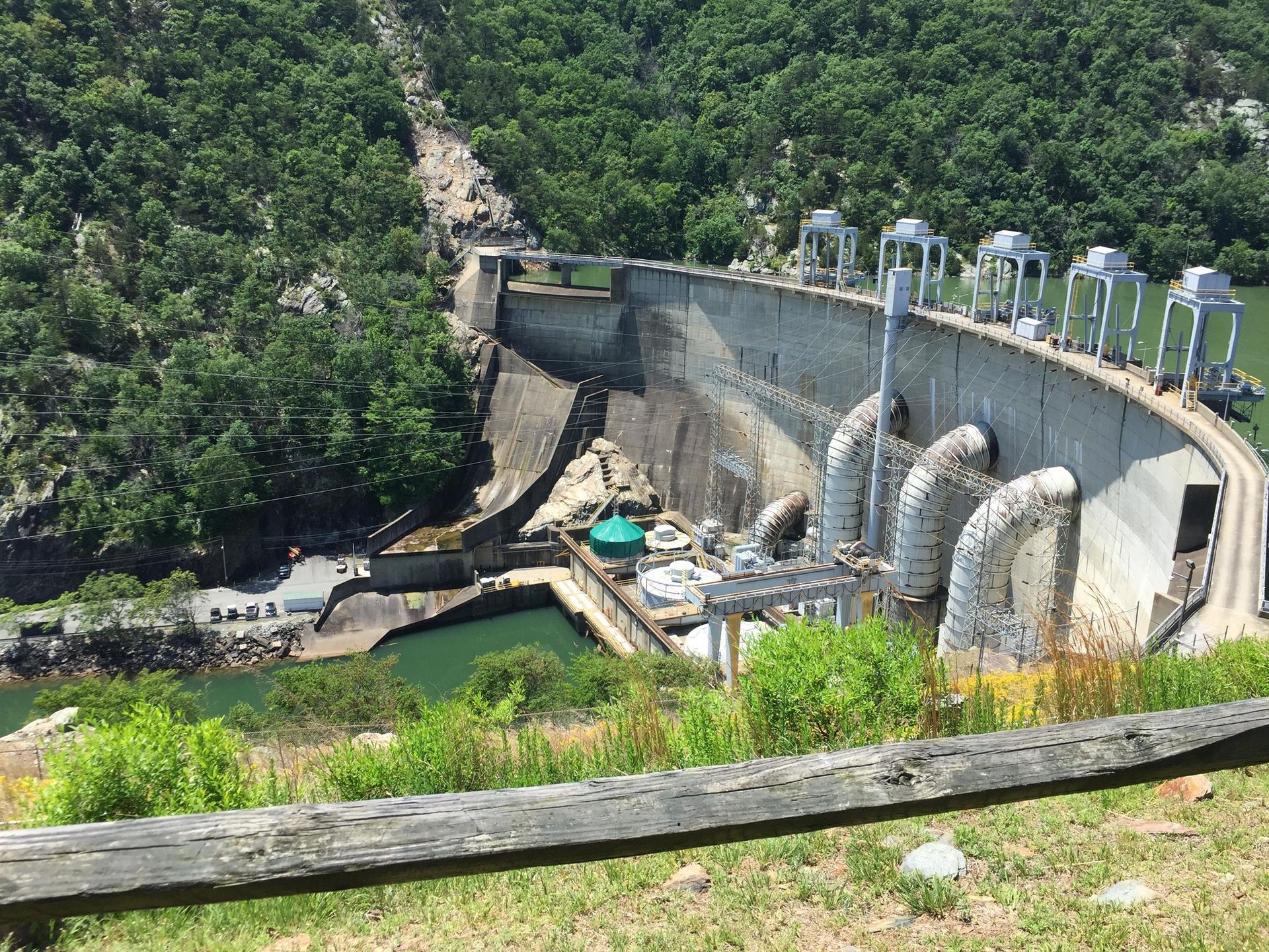 Curved concrete dam with water, surrounded by green trees and a forested hillside  at Smith Mountain Lake