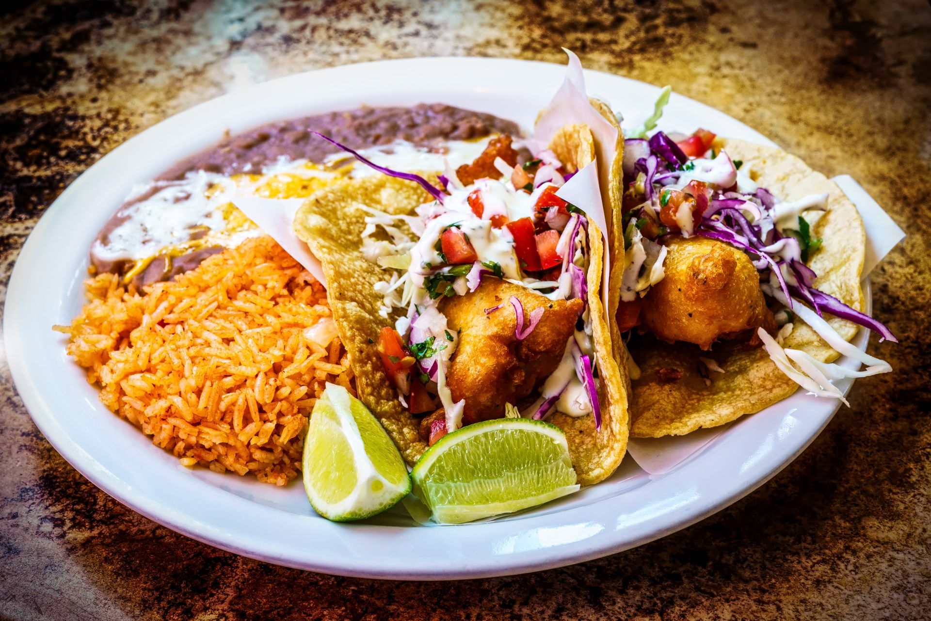 Plate of Mexican food: tacos with fillings, rice, beans, lime wedges.