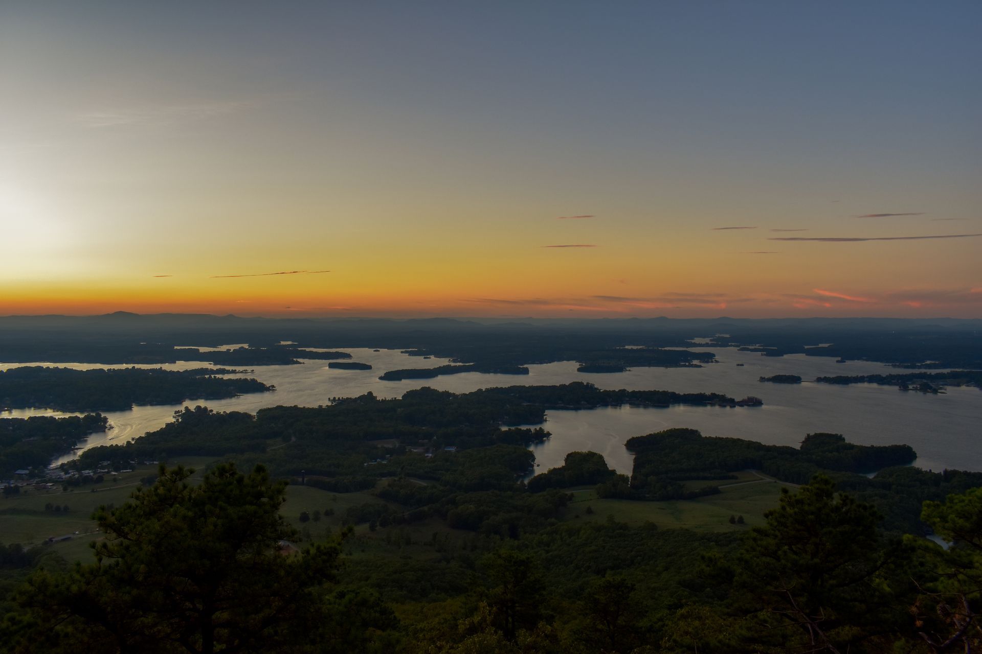 Sunset over a vast lake dotted with islands. Dark green trees contrast with the orange and blue sky.