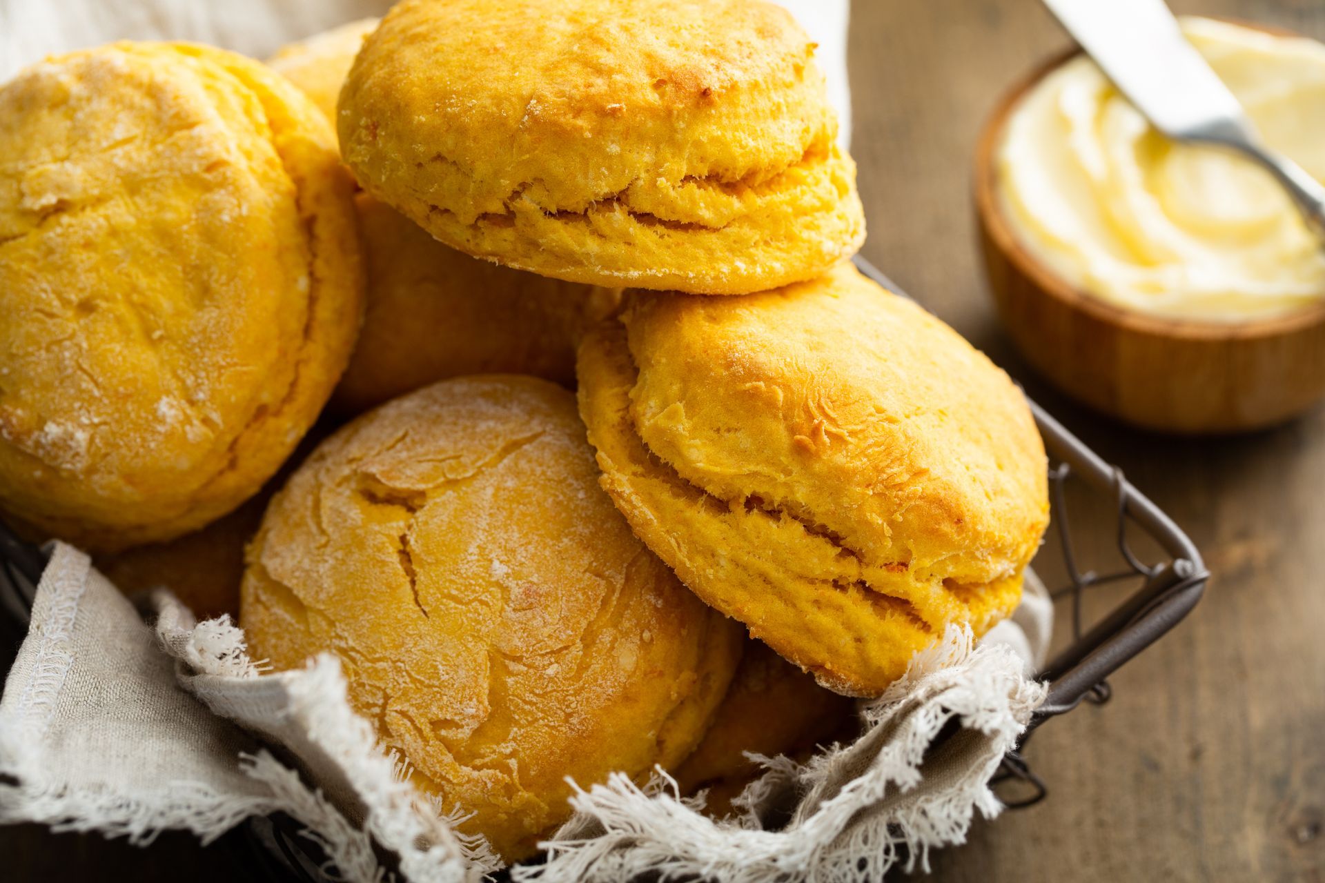 Golden biscuits in a wire basket, with butter in a wooden bowl.