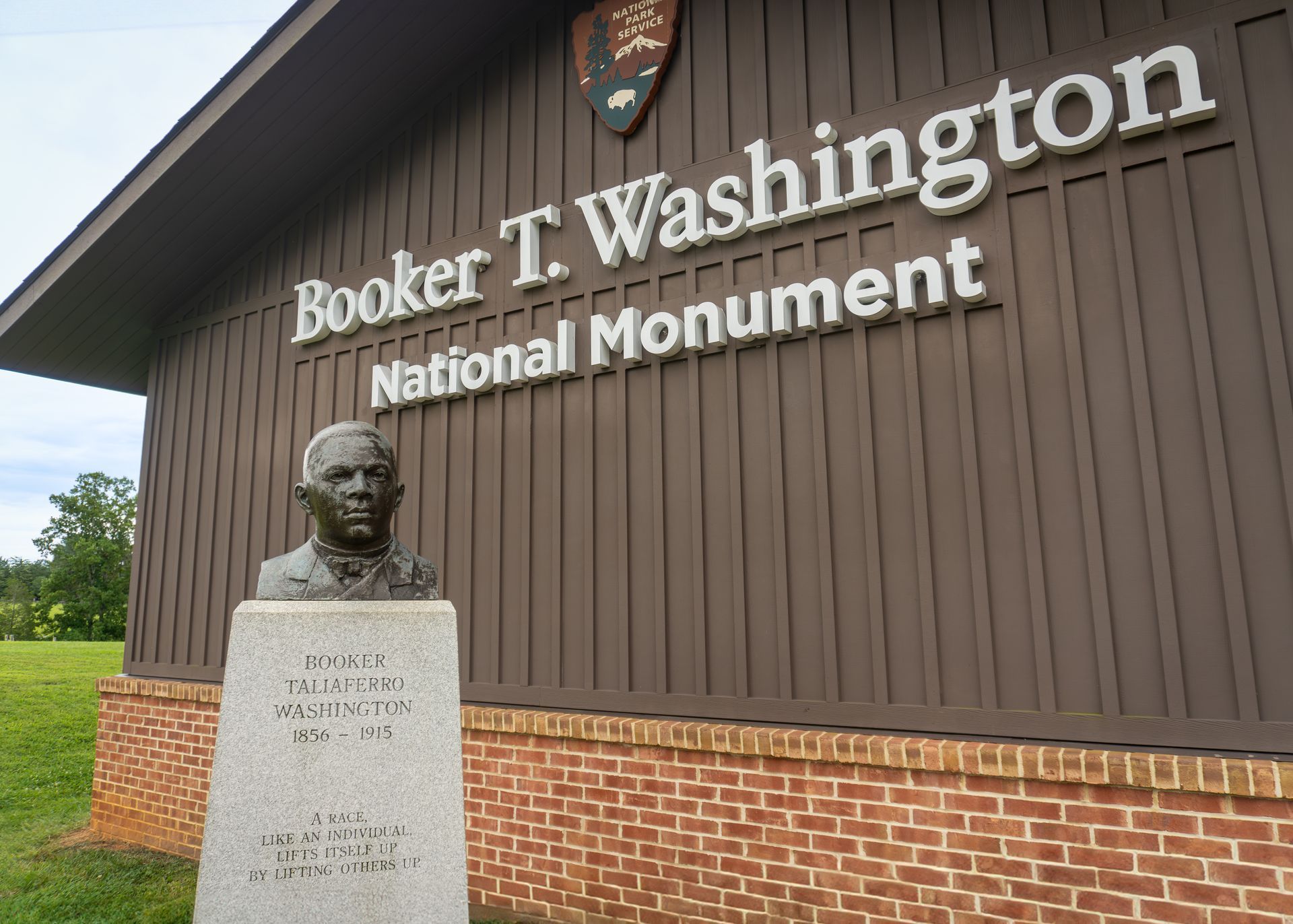 Bust of Booker T. Washington in front of the National Monument sign on a brown building with a brick base.
