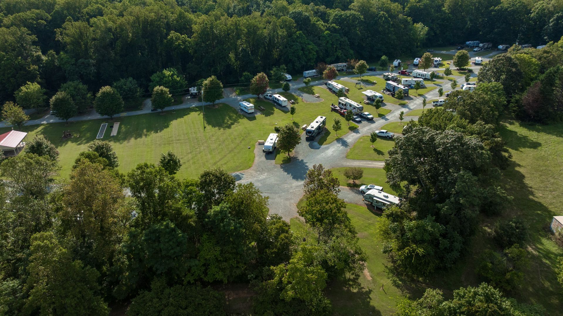Aerial view of a campground with RVs parked on grassy lots next to a forest and lake.