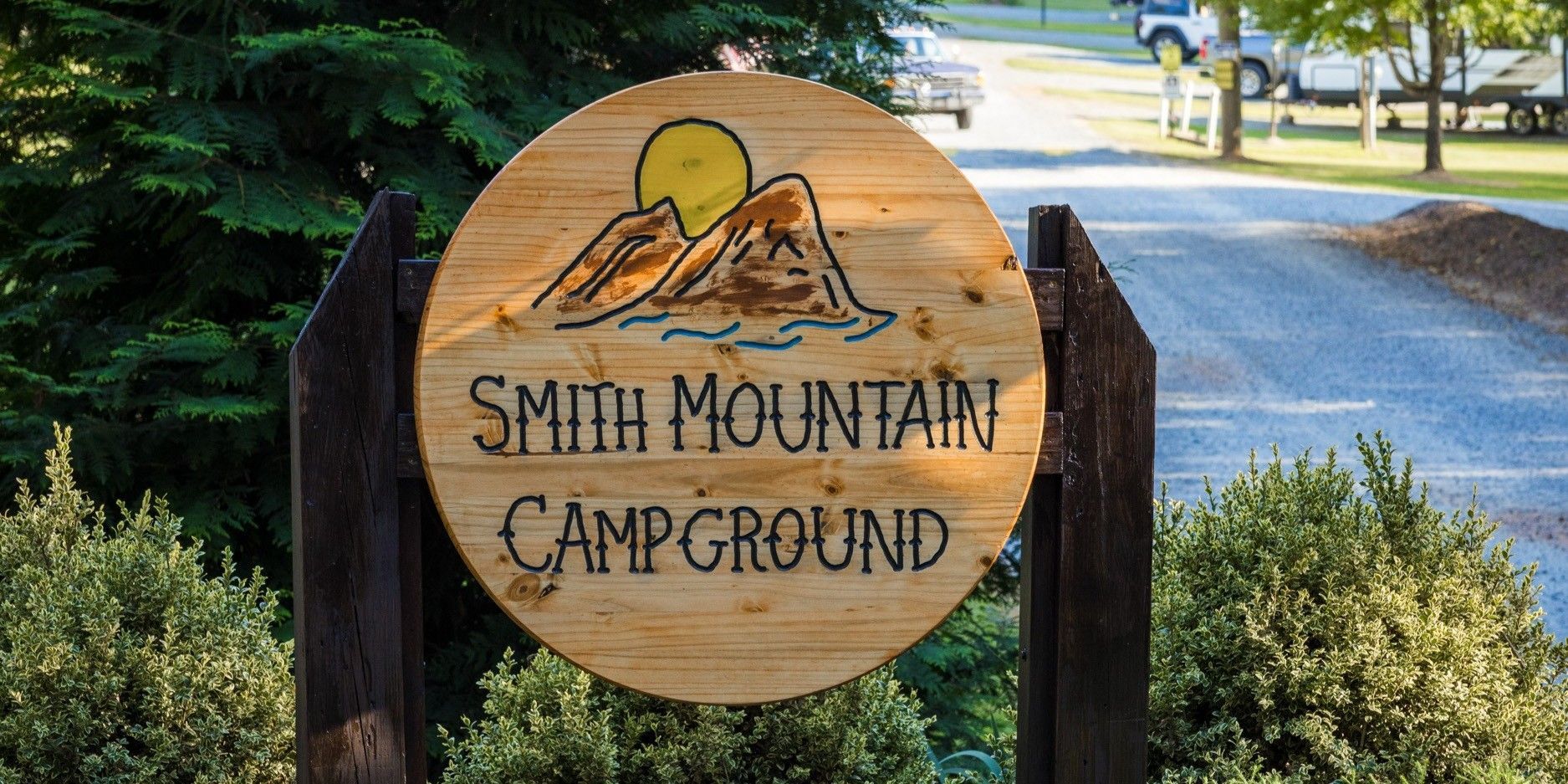 Wooden sign for Smith Mountain Campground with a mountain scene, next to a road.