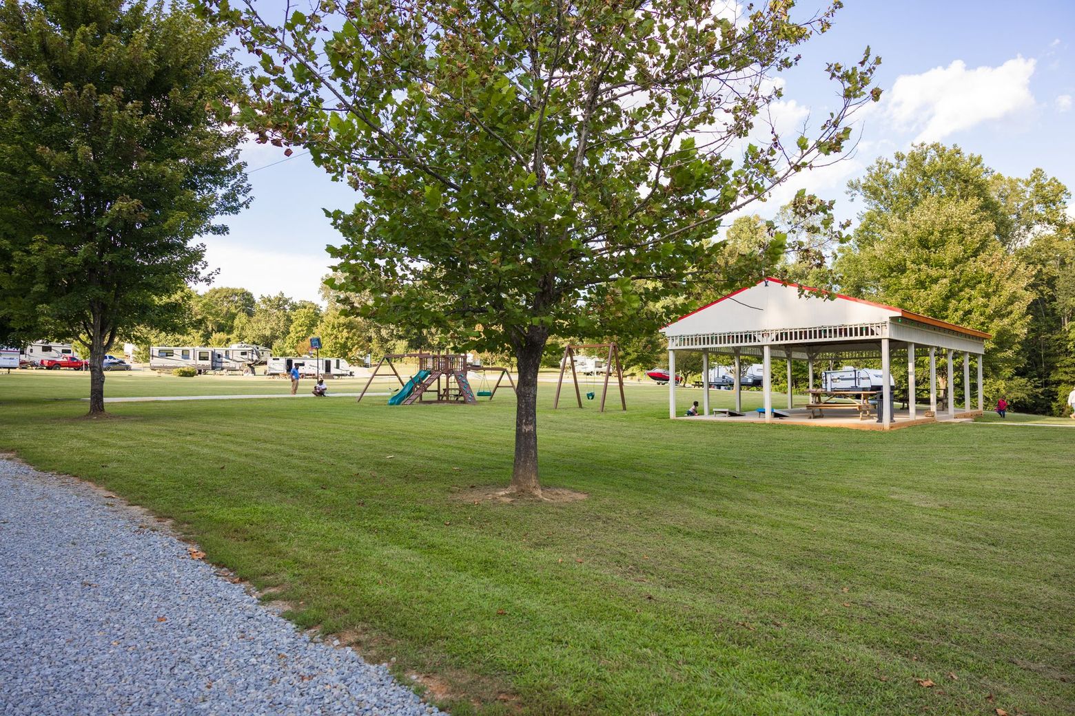 Park with playground, picnic shelter, horseshoe pits, and trees under a sunny sky.