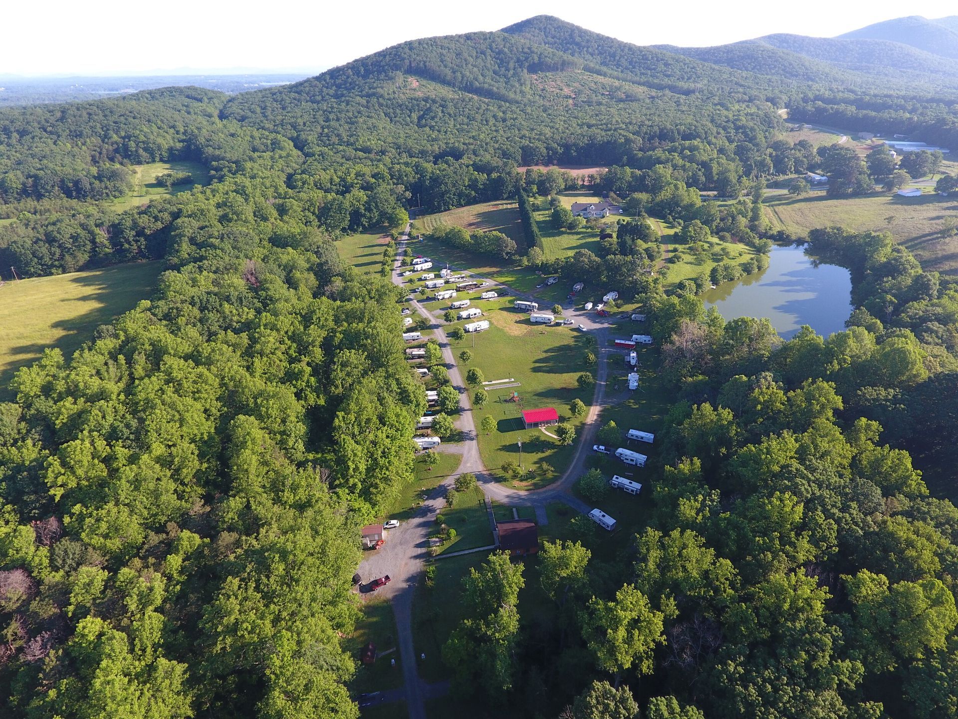 Aerial view of a campground surrounded by trees, a pond, and a mountain.