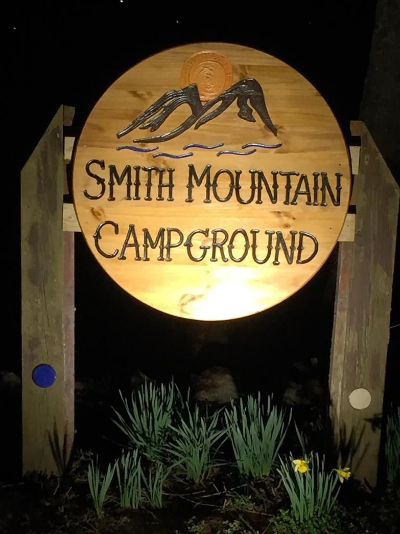 Smith Mountain Campground sign with mountain illustration; wood sign with text and surrounding foliage.
