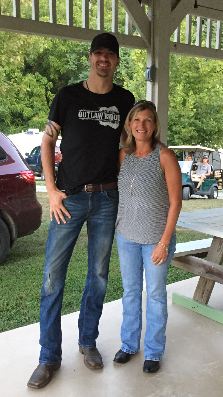 Tall man in black tee, woman in sleeveless top, standing near a picnic table outside.
