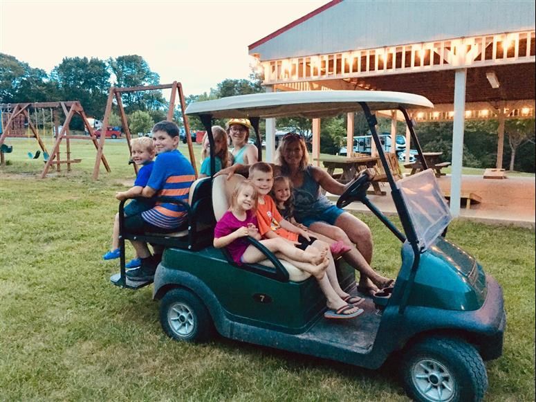 Group of people in a green golf cart; children and adult smiling outdoors.