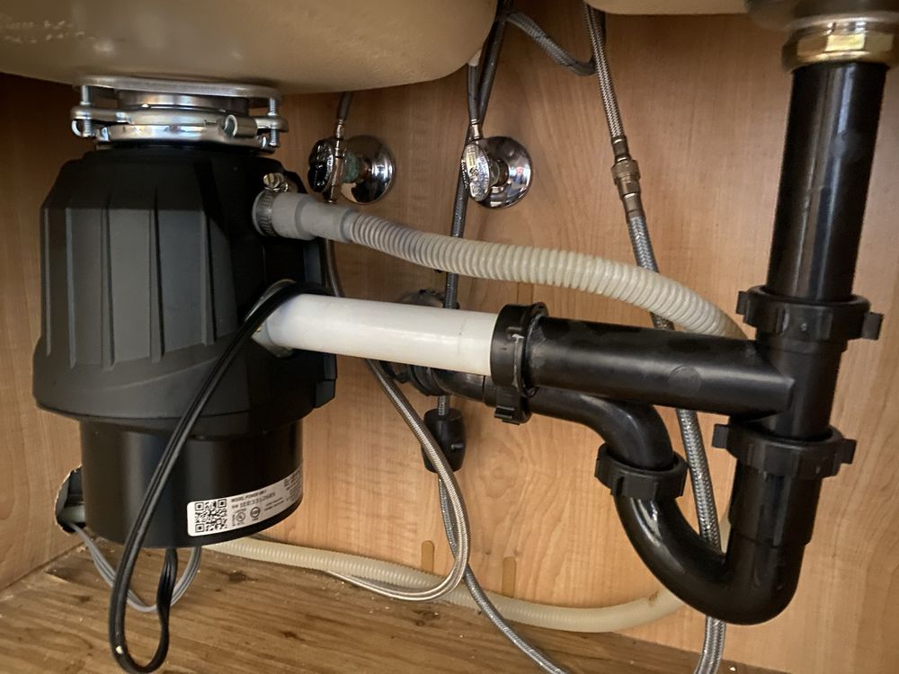 Under-sink plumbing with a black garbage disposal and drain pipes, connected to a white sink.