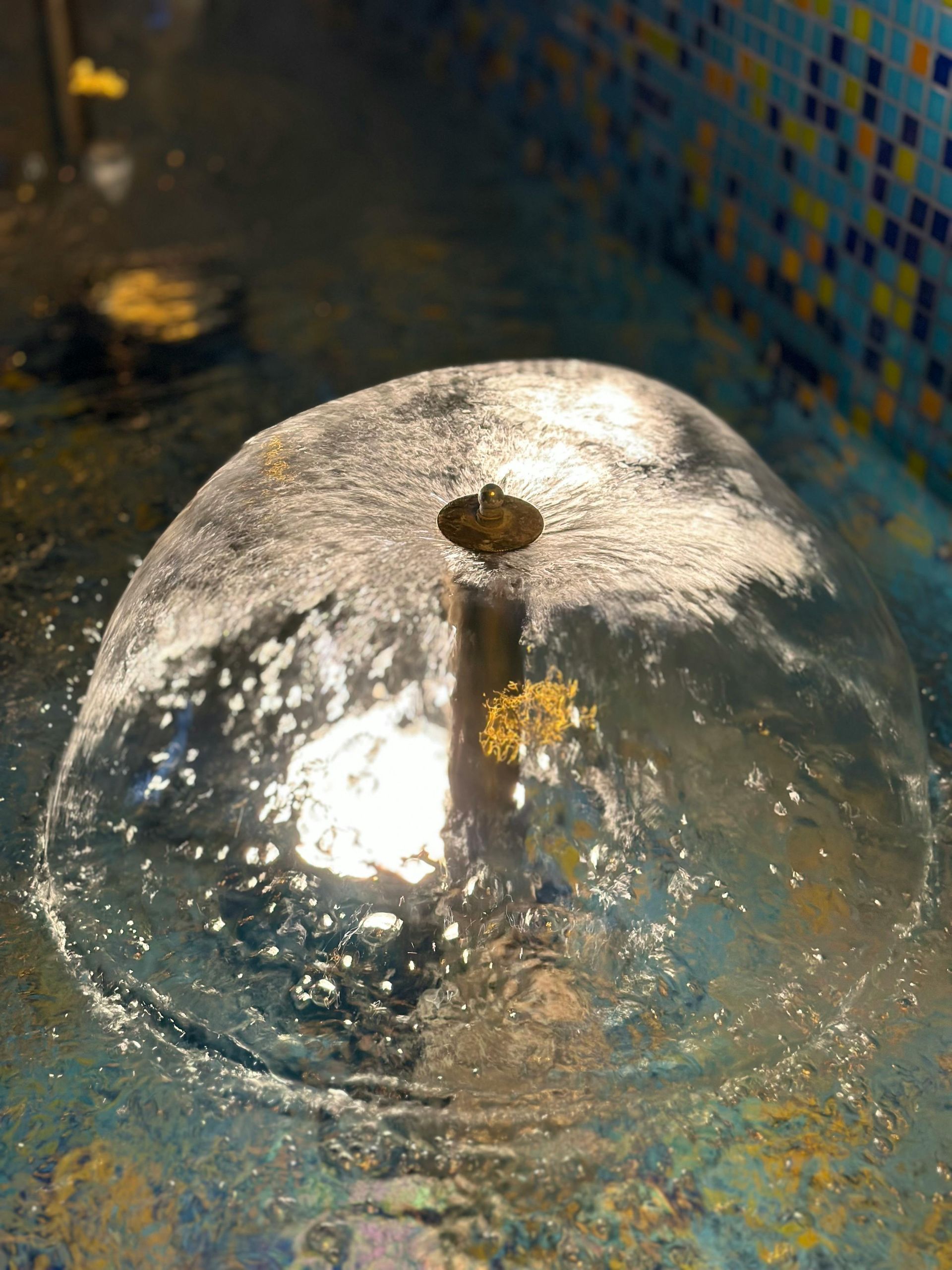 Water fountain with a dome of water spraying up from a central nozzle, pool with blue tile.