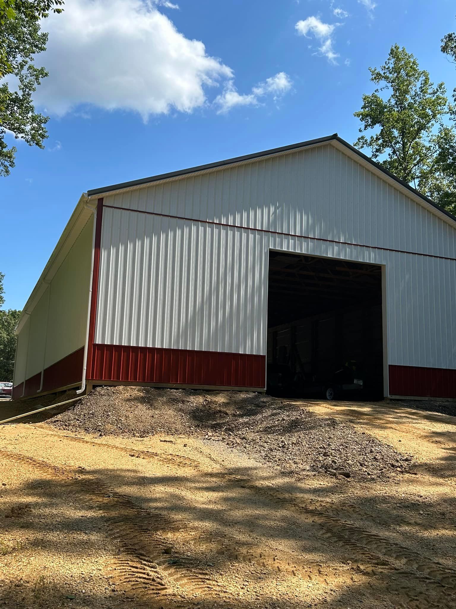 A large metal white barn with a red trim is sitting in the middle of a dirt field.