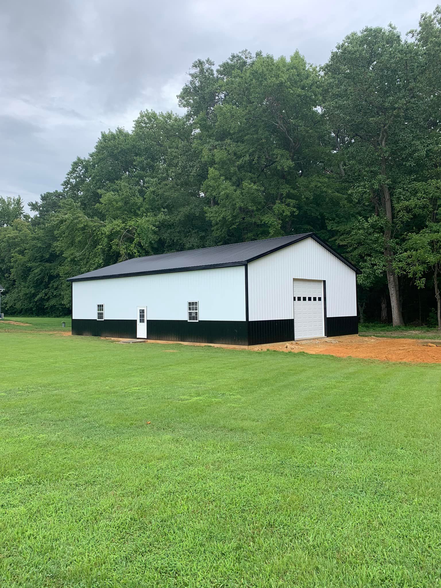 A white and black metal barn is sitting in the middle of a grassy field.