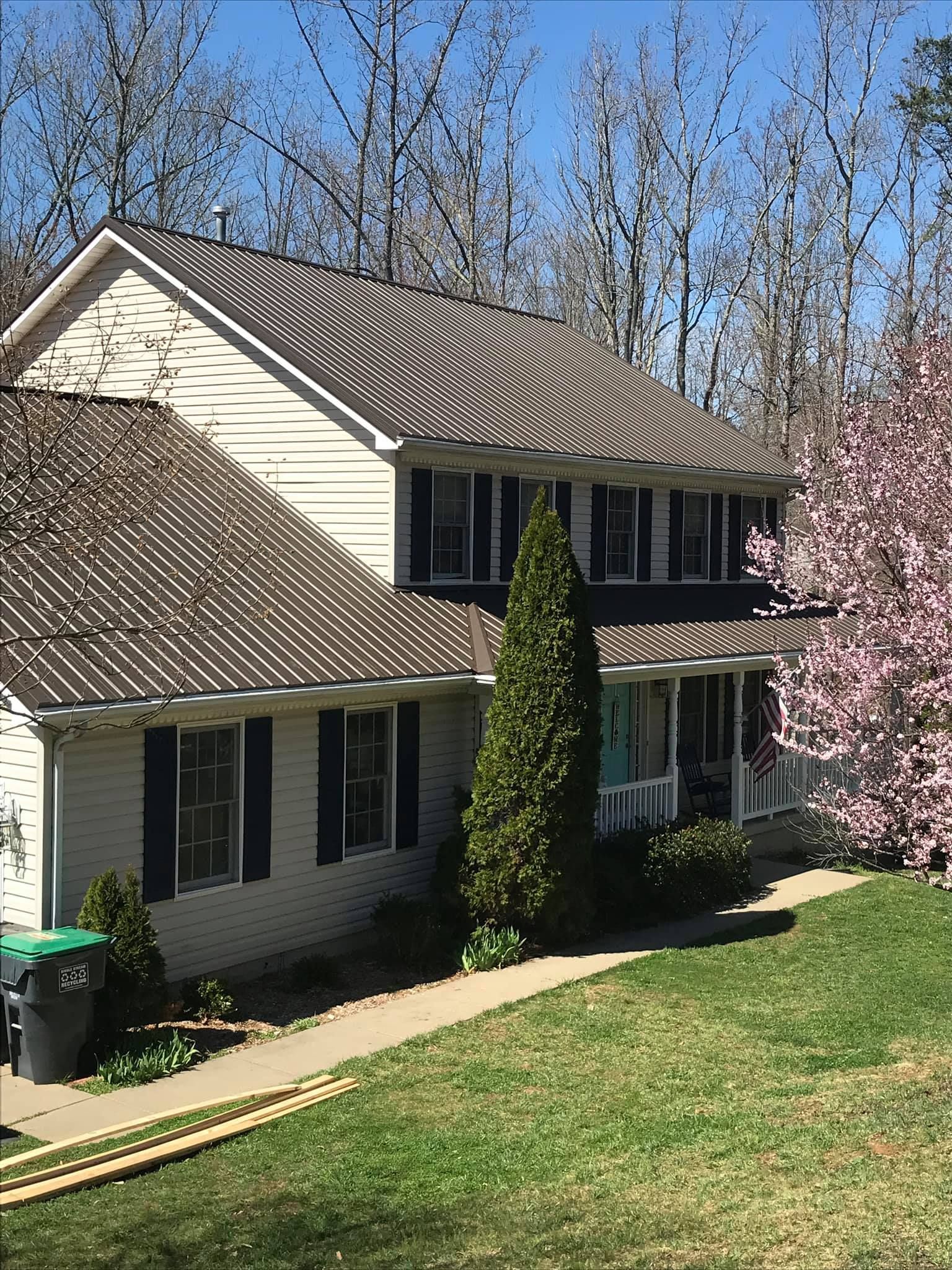 A white house with a brown metal roof is surrounded by trees.
