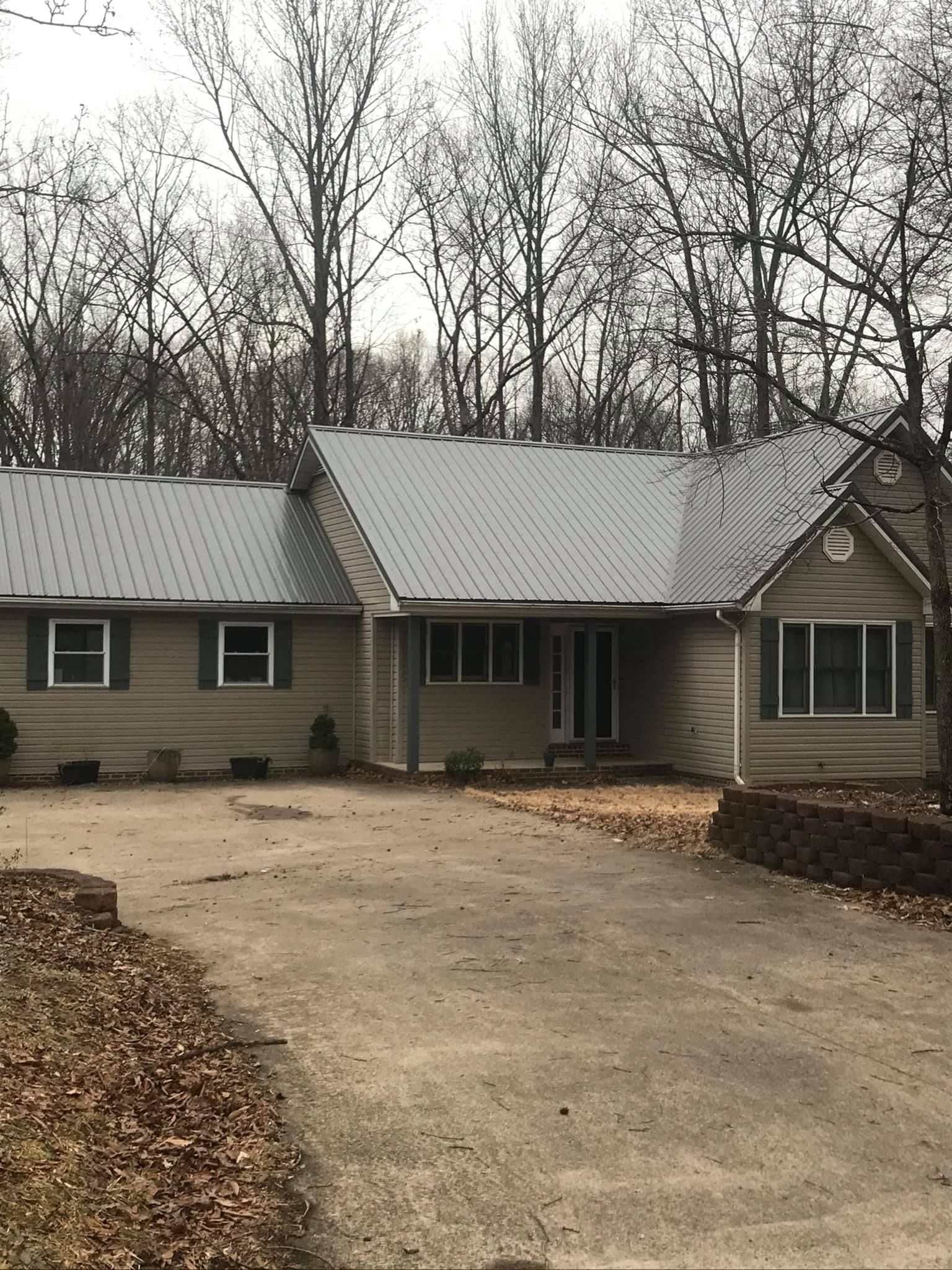 A house with a metal roof is surrounded by trees on a cloudy day.