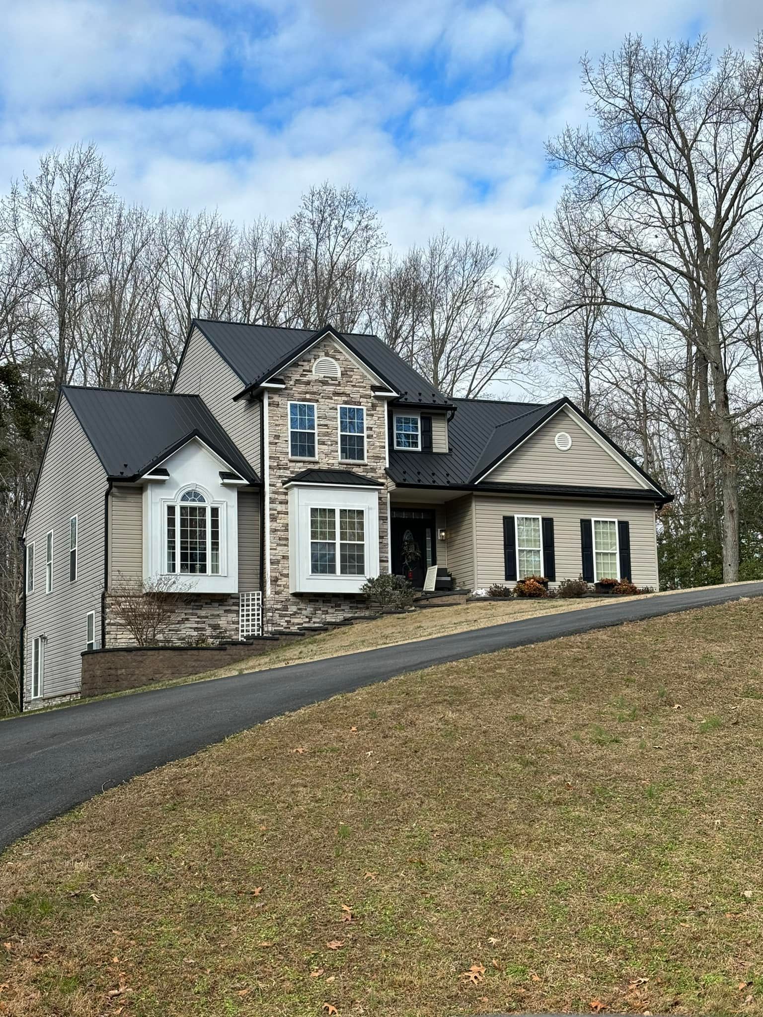 A large house with a black roof is sitting on top of a hill.