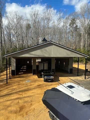 A car is parked in a pole barn constructed garage next to a boat.