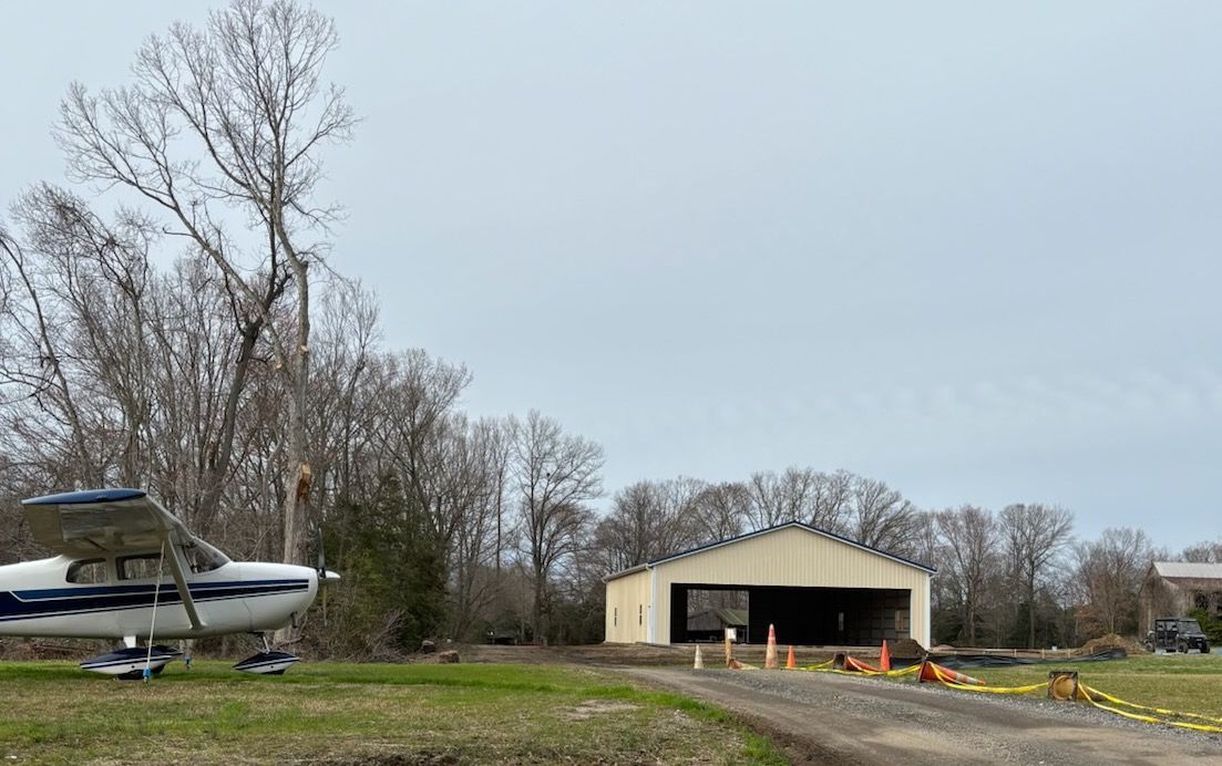 A small plane is parked in front of a hangar, pole barn construction.