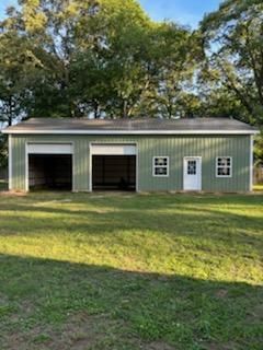 A green garage with two doors is sitting in the middle of a grassy field.