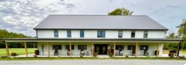 White building with gray roof, covered porch, windows, and a green lawn.